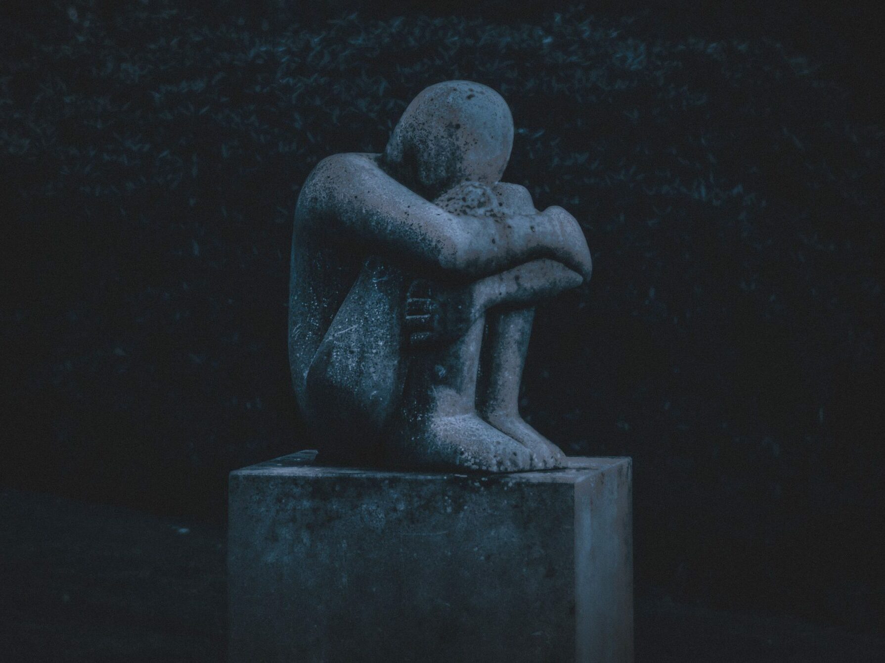sculpture of man holding knees and crying
